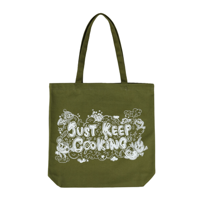 An olive green canvas tote bag with two handles, featuring a white graphic print on the front that reads 'Just Keep Cooking' surrounded by doodles of food and kitchen items, set against a plain white background.